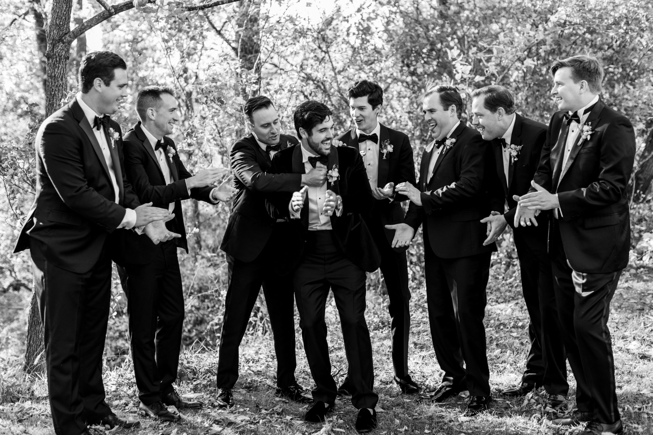 Groom and groomsmen laugh and smile outside in black tuxedos for Clifton wedding photography