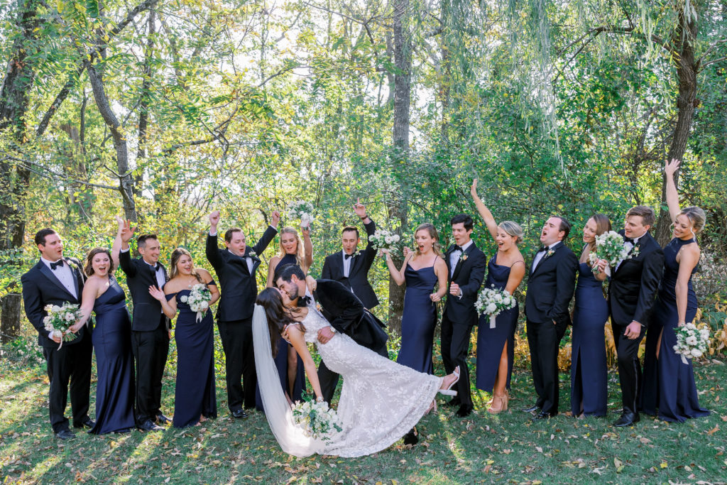 Bridal party cheers for bride and groom as they dip kiss outisdee 