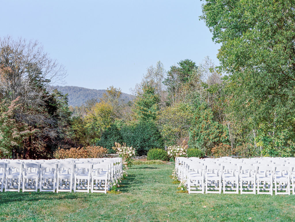 White chairs outside at wedding venue on the lawn with greenery 