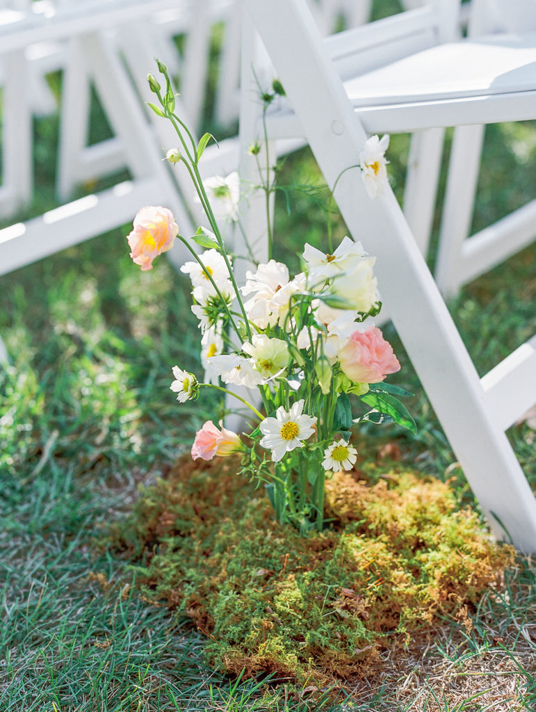 White and pink flowers on a bed of moss at the end of seats at venue 