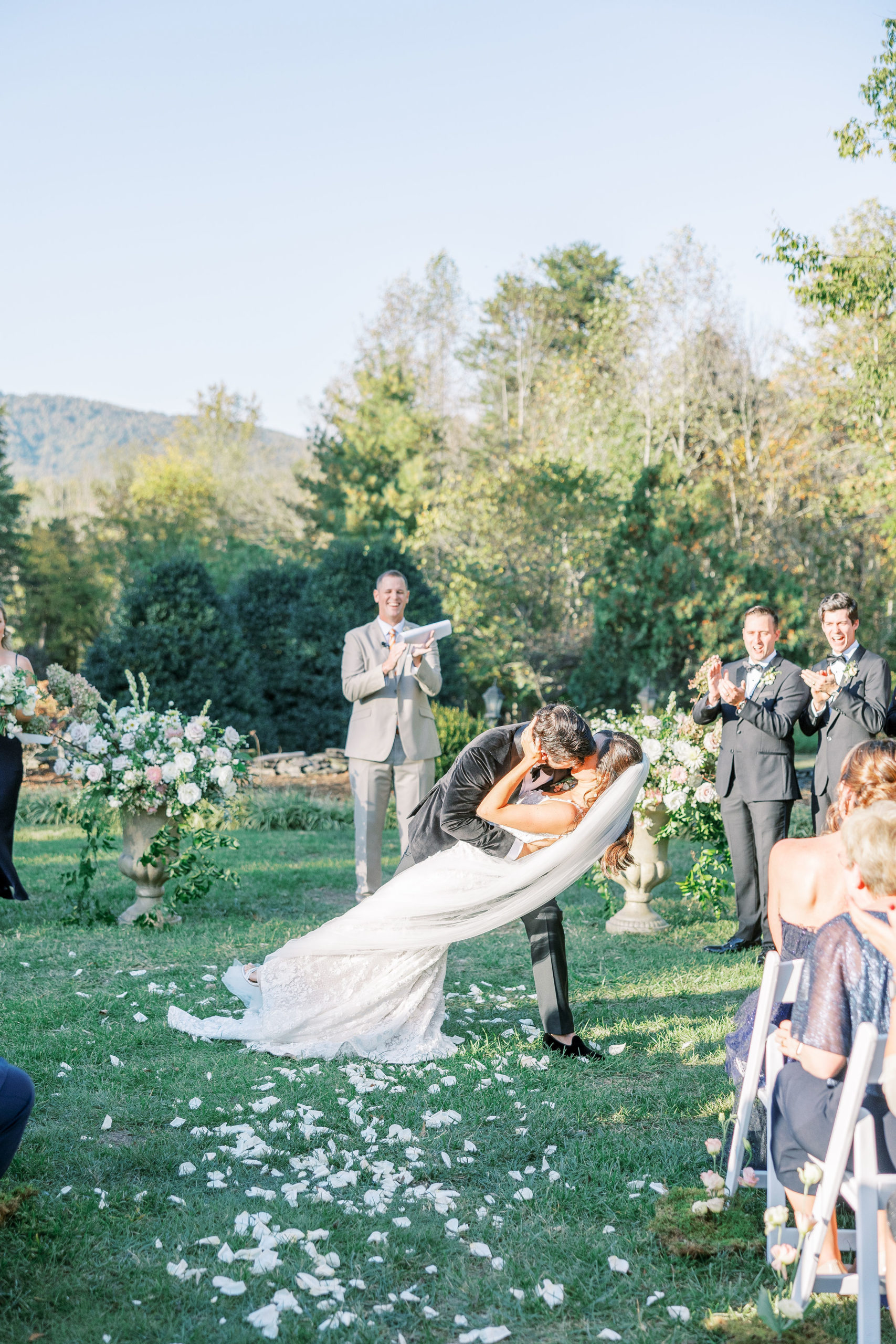 At the altar outside, groom dip kisses wife with guests smiling and clapping for Clifton wedding photography