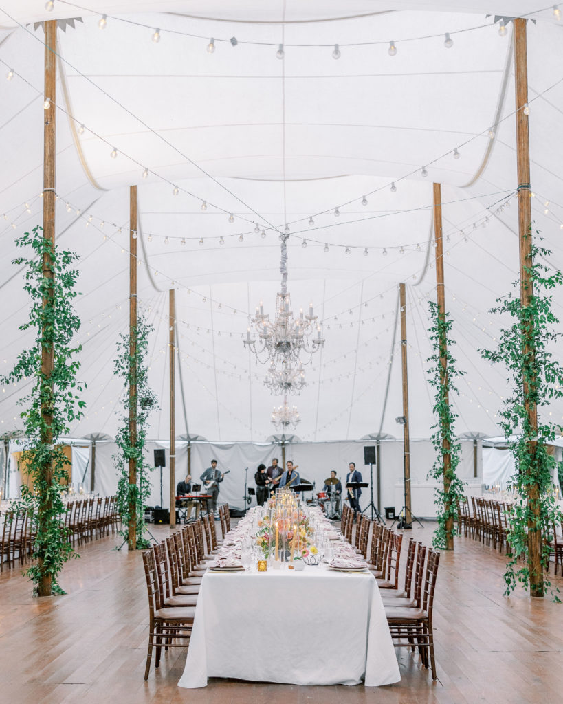Wedding reception underneath tall white tent with tall pieces of wood holding it up, string lights , and long white tables for Clifton wedding photography