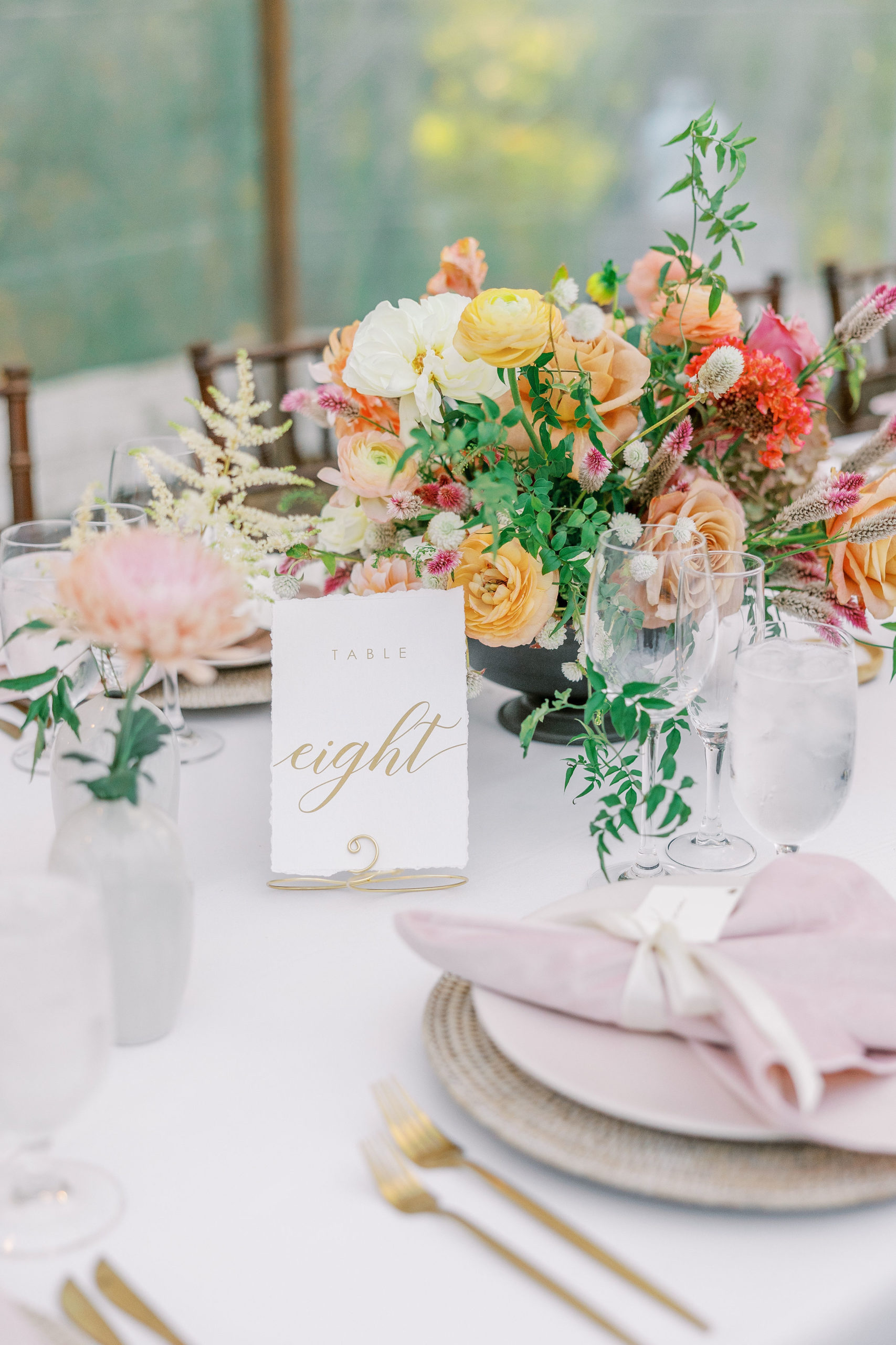 Close view of yellow, pink, and peach flower centerpieces with table eight place card on white paper and gold calligraphy for Clifton wedding photography 