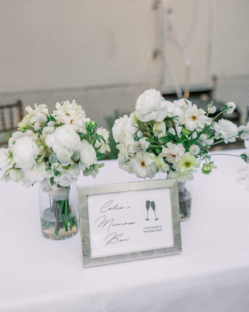 Frame that writes "Celia's Mimosa Bar" on table with white flowers behind for Clifton wedding photography
