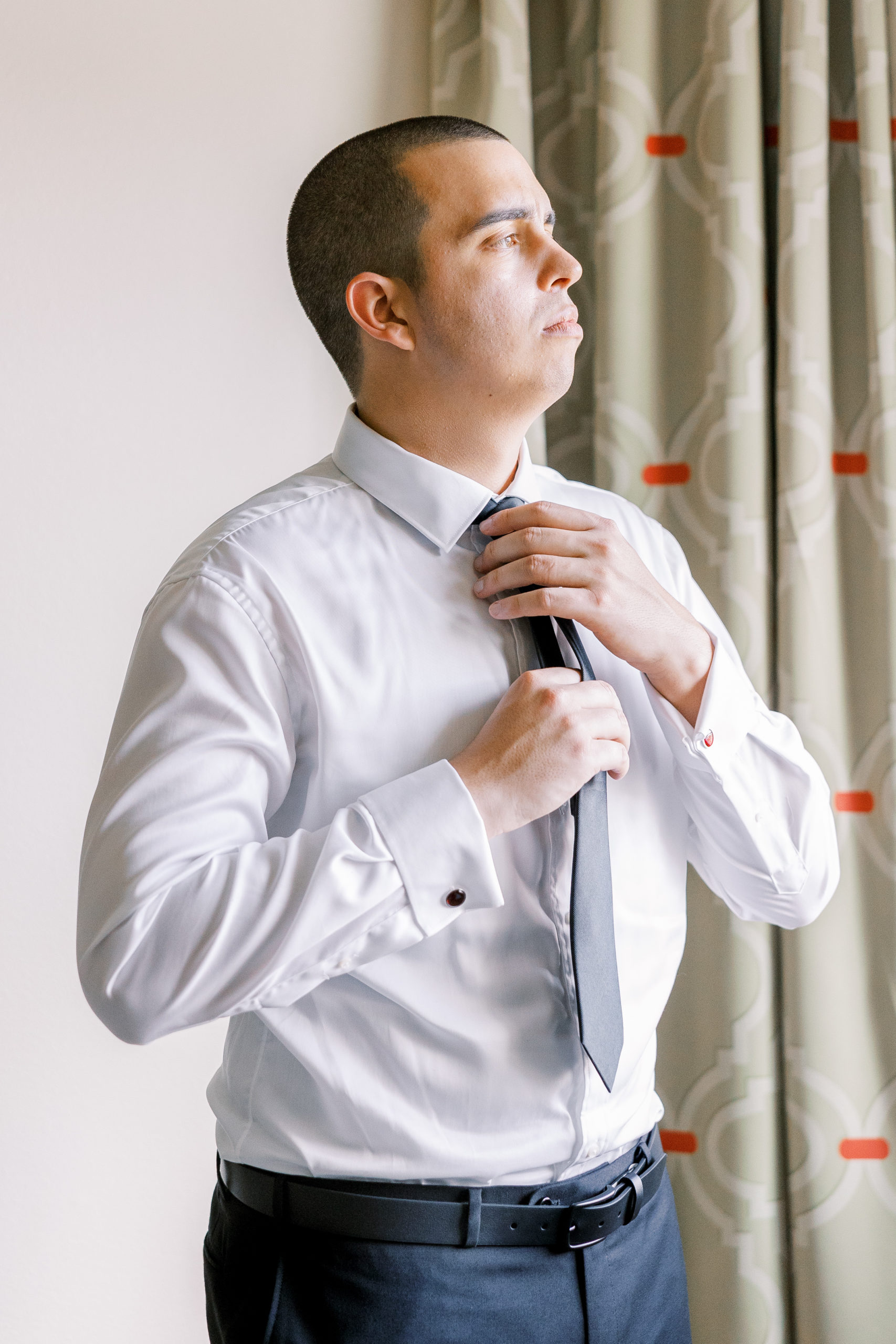 Groom adjusts tie and looks out the window for California Grill Wedding