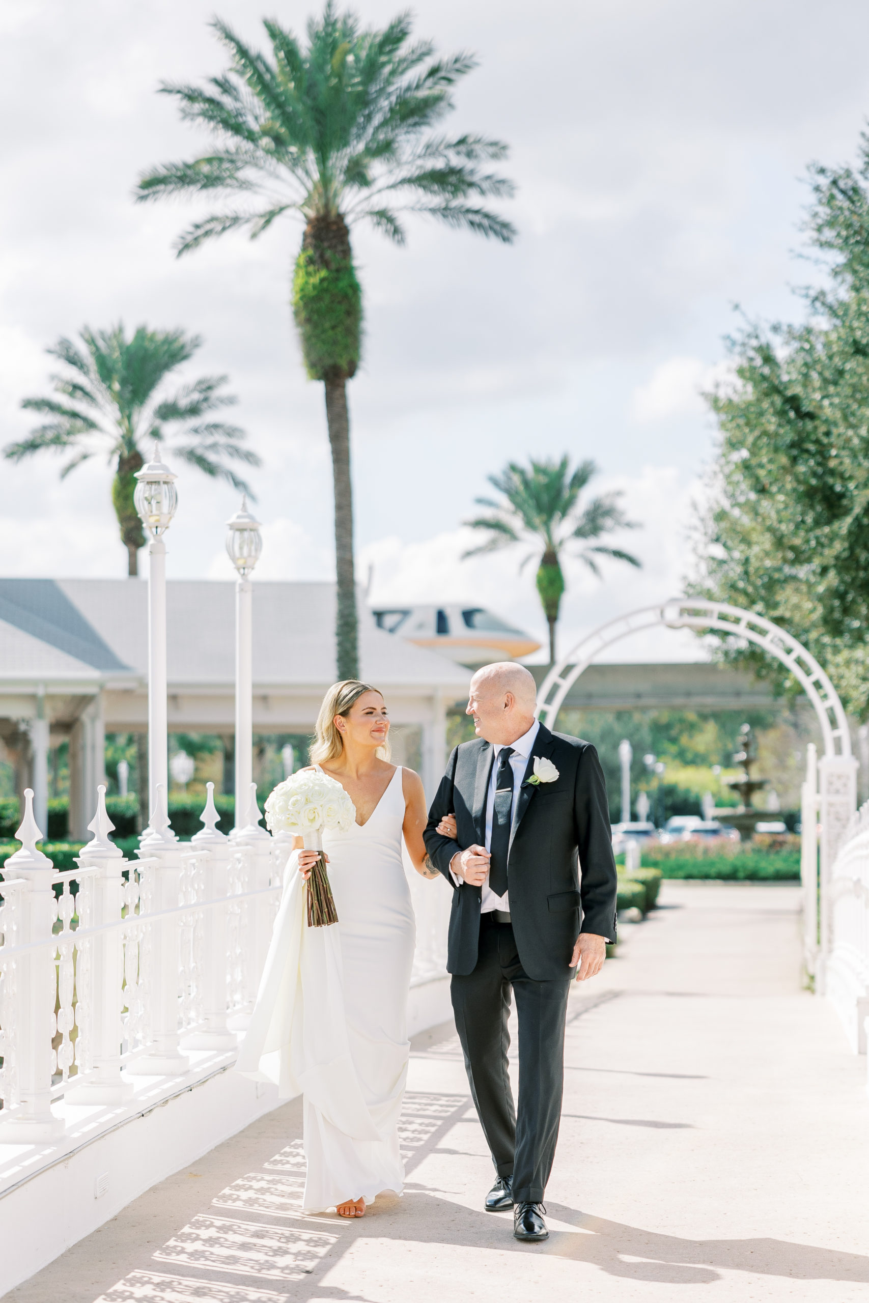 Father of bride and daughter walk over white bridge toward wedding pavilion for Disney Film Wedding Photographer
