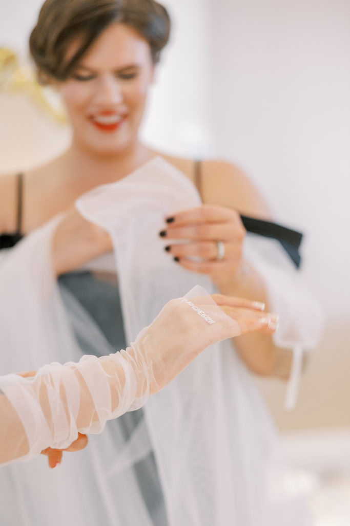 Bride puts on wedding sleeve gloves with help of bridesmaid 