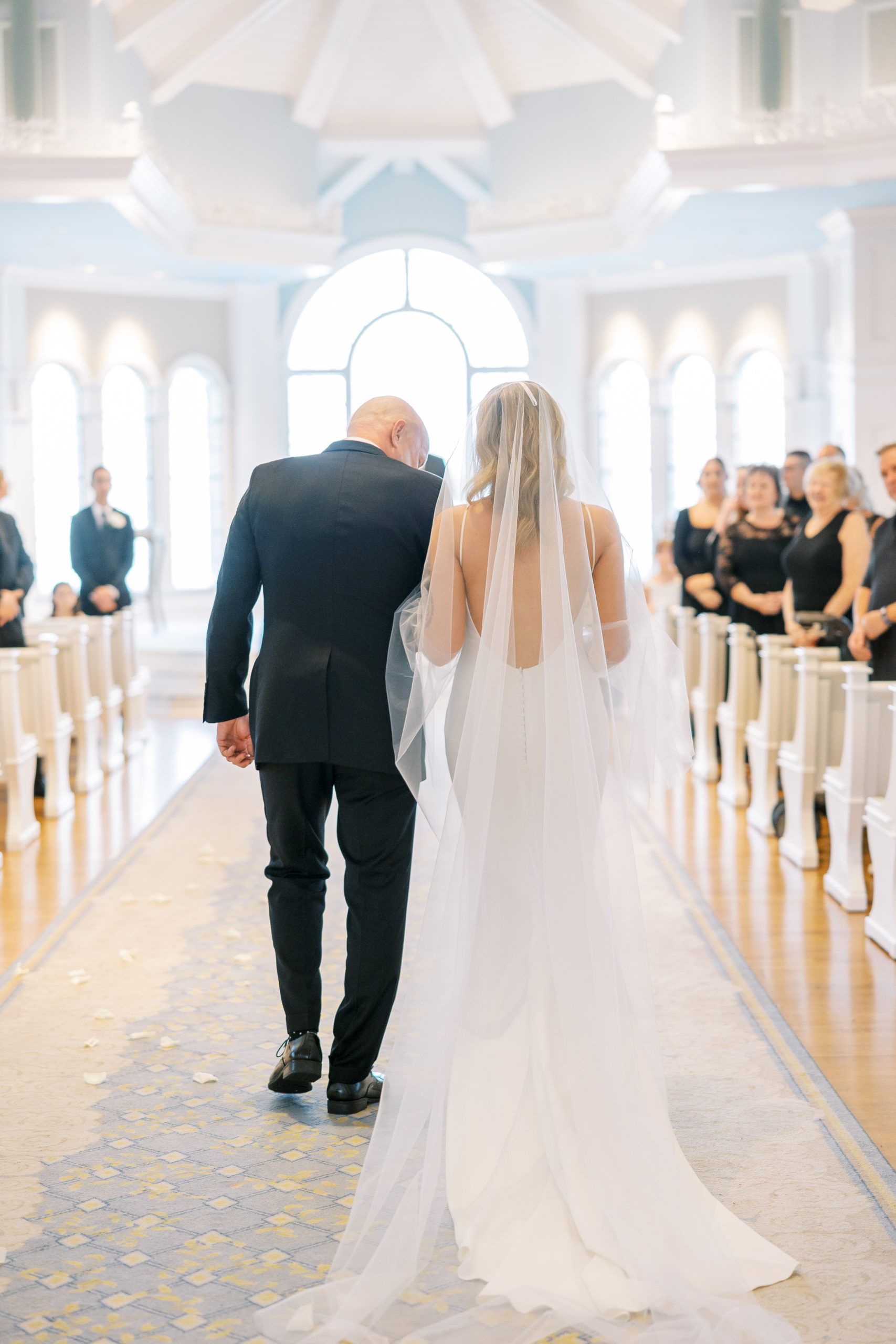 Father of the bride walks daughter down the aisle in white and blue wedding pavilion for Disney Film Wedding Photographer