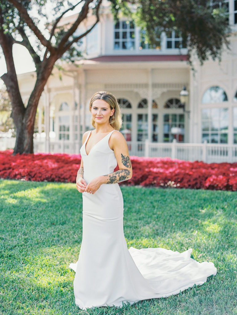 Bride poses on lawn with red flowers in the background 