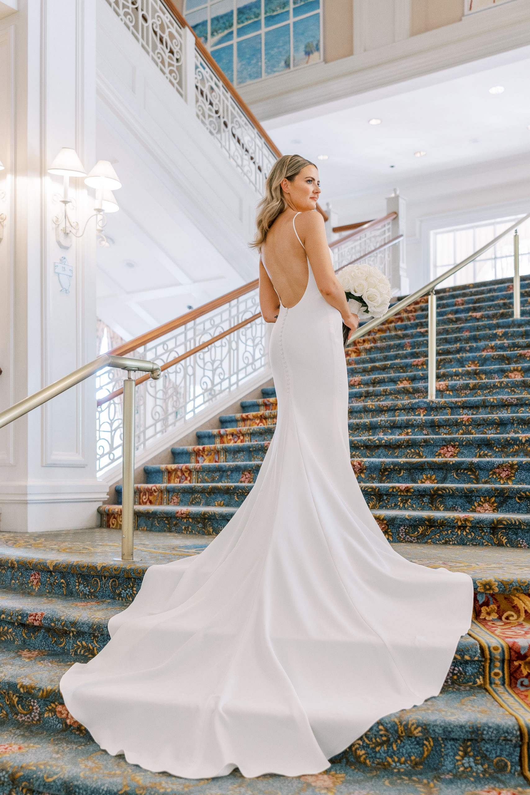 Bride holds ivory rose bouquet and looks to the side with grand staircase for Disney Film Wedding Photographer  