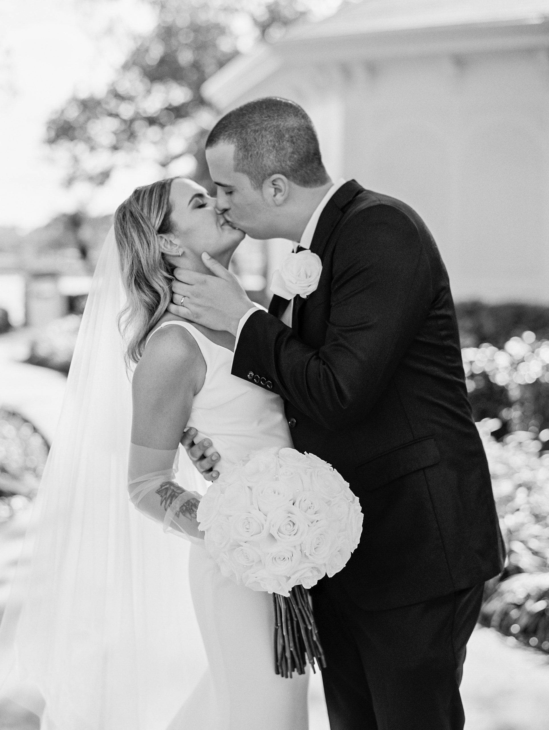 Black and white picture of bride and groom kissing, holding white rose bouquet for Disney Film Wedding Photographer