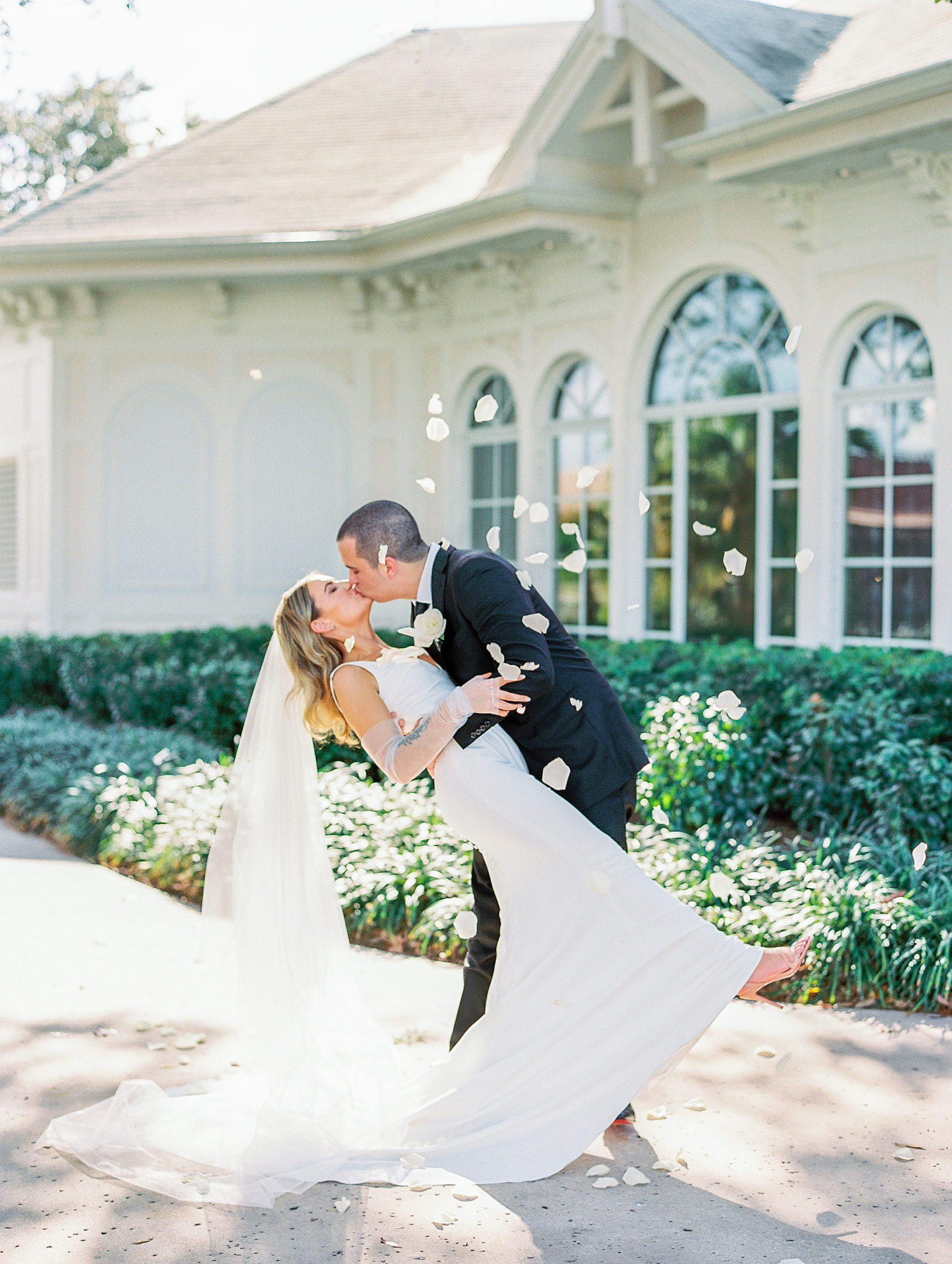 Groom dips bride and kisses her as white rose petals fall over them for Disney Film Wedding Photographer