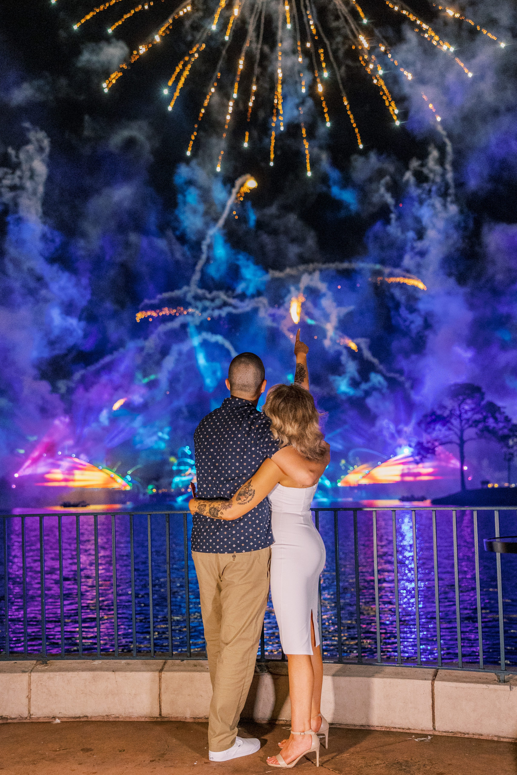 Couple watches and points at golden fireworks with blue and purple lights for California Grill Wedding