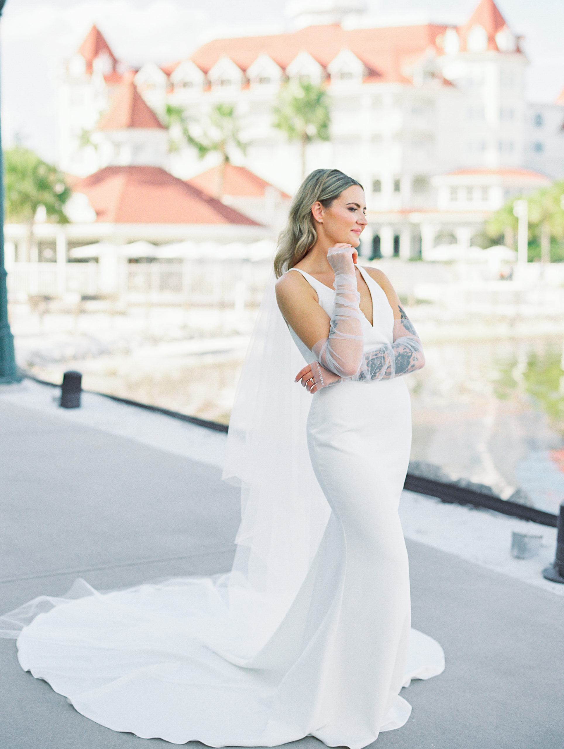 Bride poses with chin on hand and looks away with white and orange resort in background for California Grill Wedding
