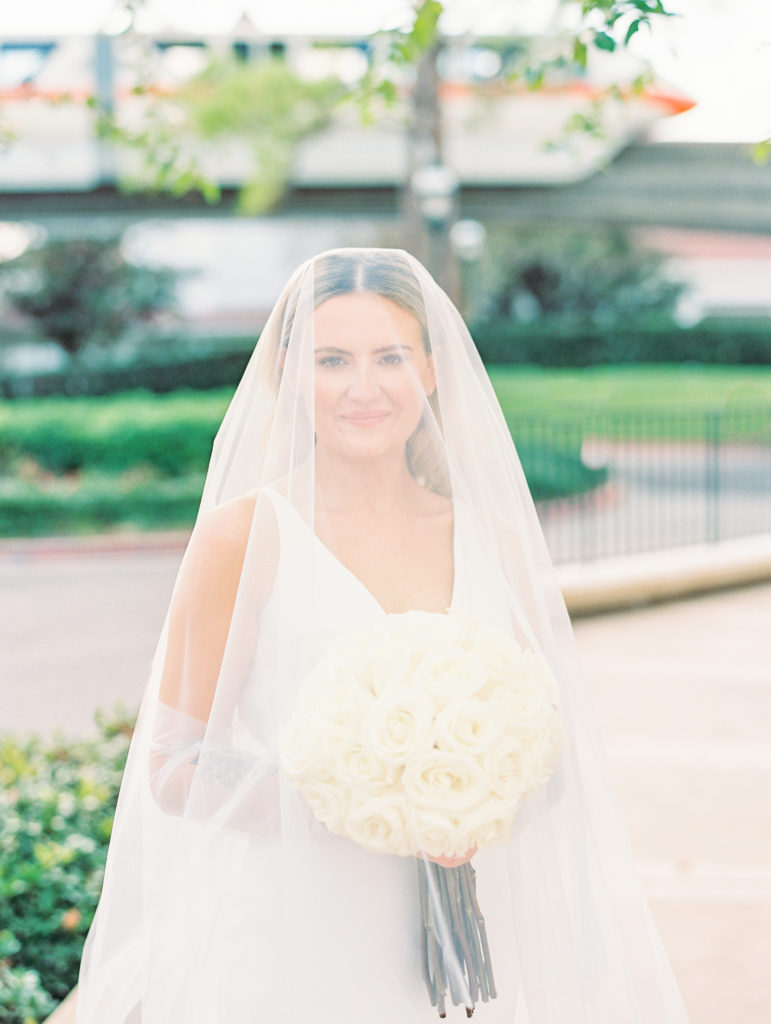 Bride poses with veil over head holding white rose bouquet 