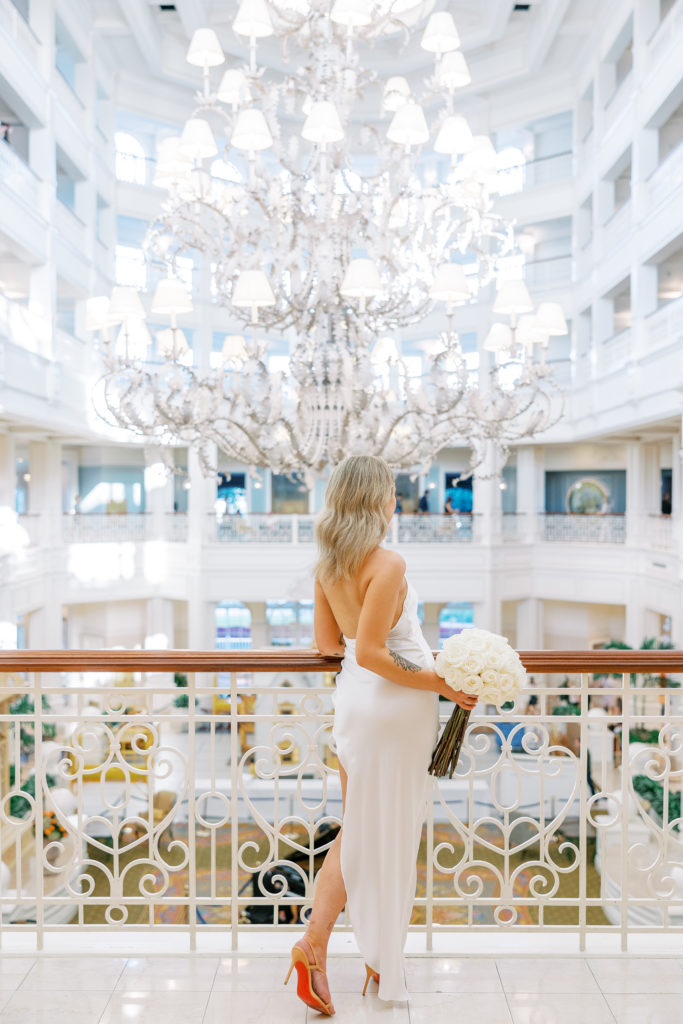 Bride turns away holding white rose bouquet with large chandelier in background for Disney Film Wedding Photographer