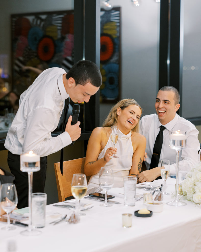 Bride and groom sit and laugh during speech at wedding reception 
