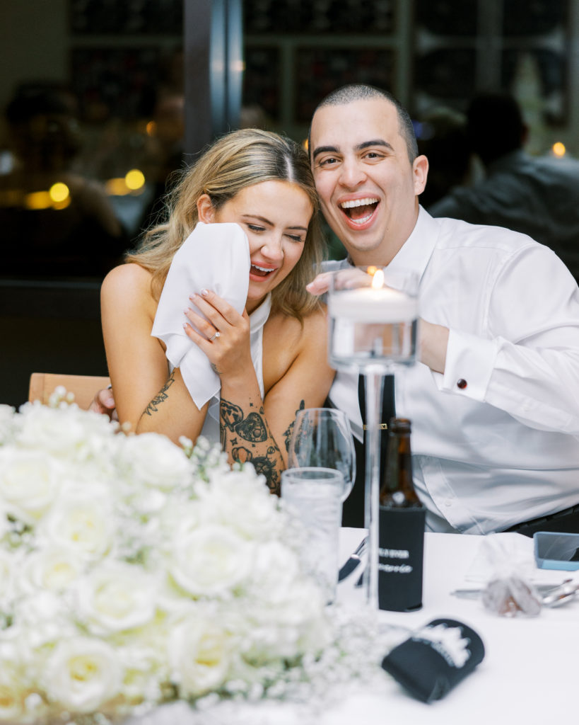 Bride wipes away tears with napkin and groom smiles during wedding reception for California Grill Wedding