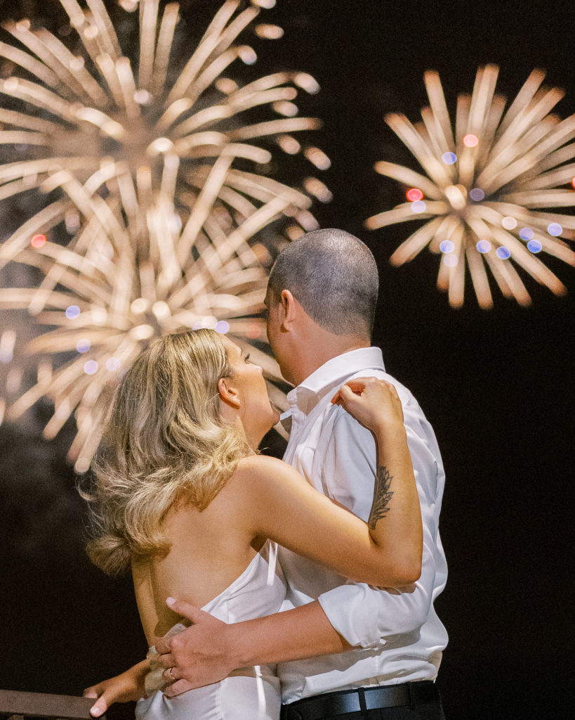 Bride and groom embrace and watch gold fireworks in the sky during reception 