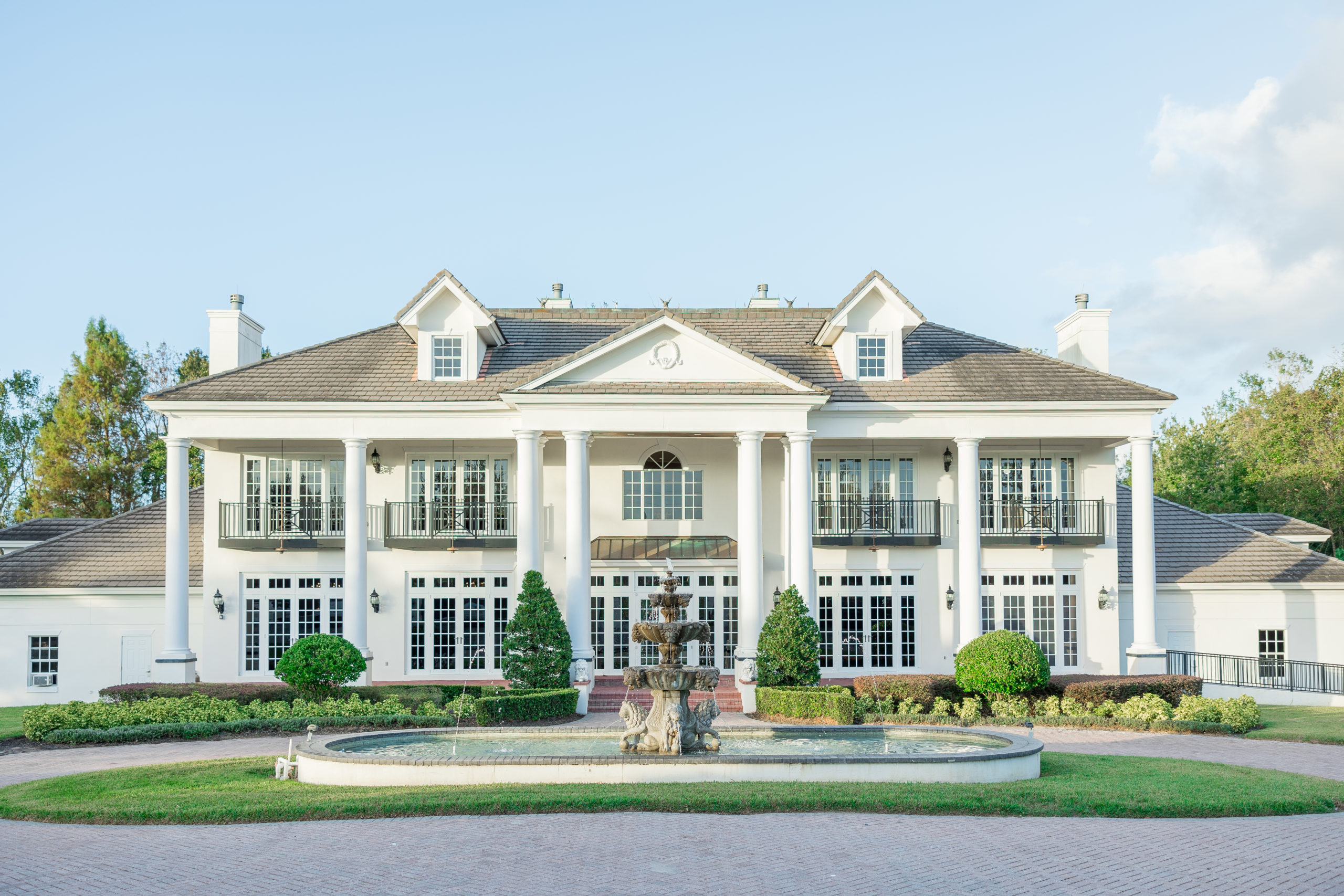 White estate with columns and fountain in the middle of the driveway with fresh cut lawn for Luxmore Grande Wedding