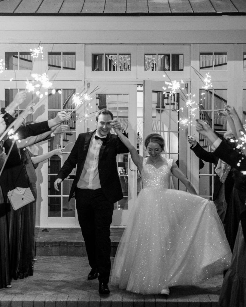 Bride and groom hold up hands and walk through send off with sparklers 
