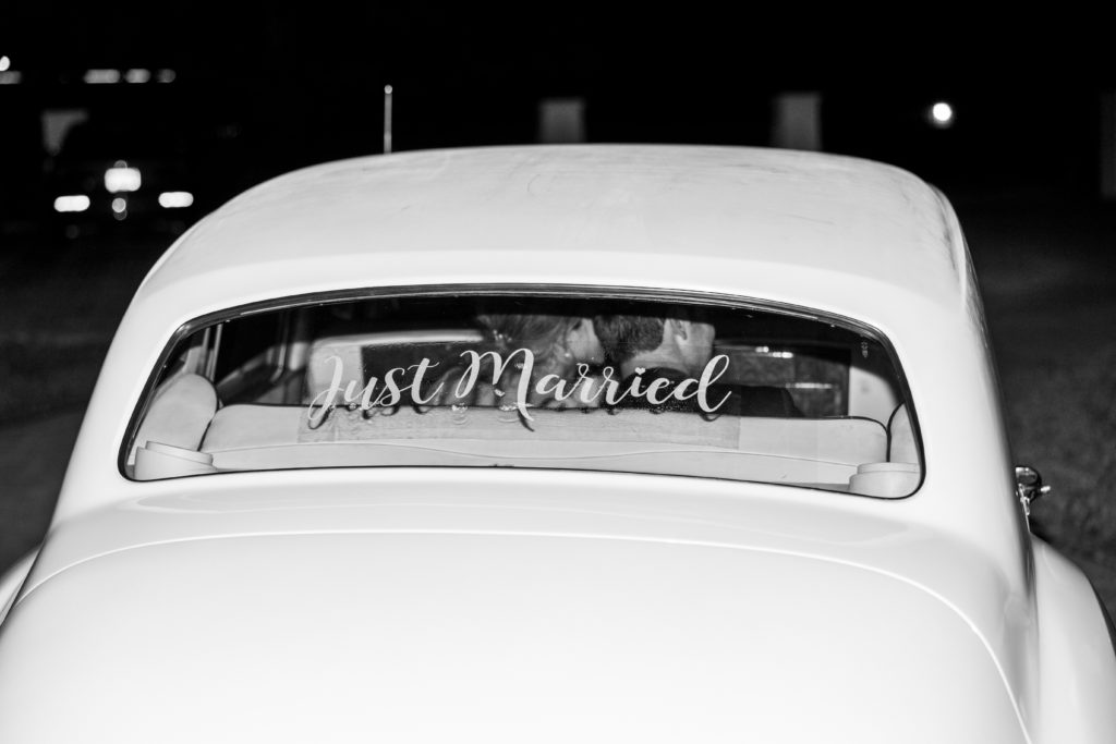 Bride and groom sit in vintage car and drive away with "just married " written for Luxmore Grande Wedding