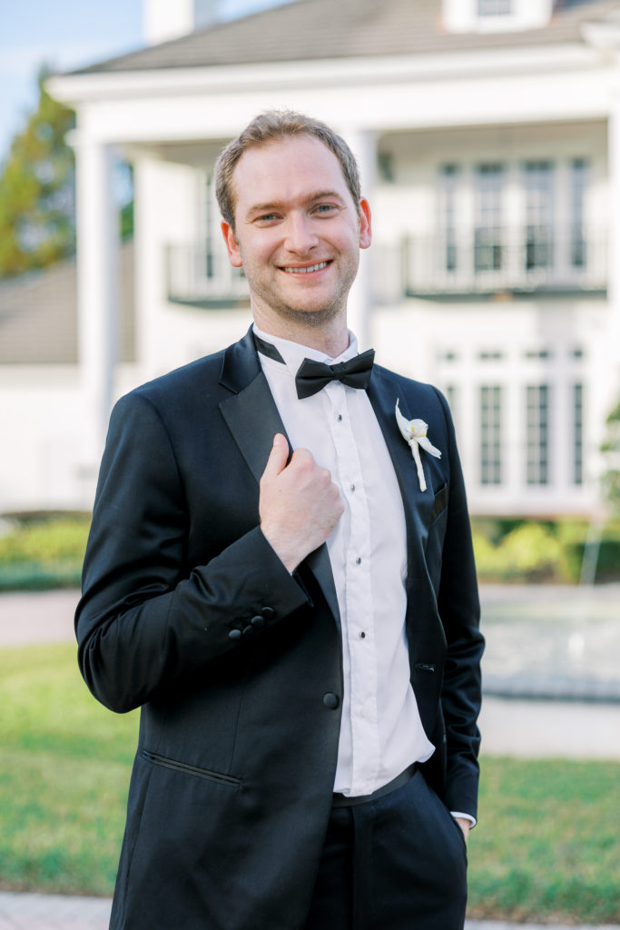 Groom poses and smiles wearing a black tuxedo and bowtie for Luxmore Grande Wedding
