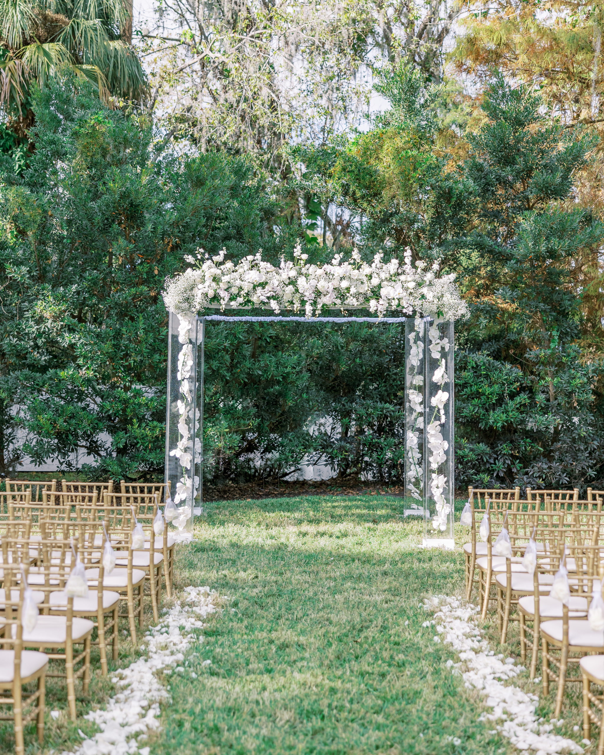Wedding ceremony outside with gold chairs and large wedding arch with white flowers for Luxmore Grande Wedding
