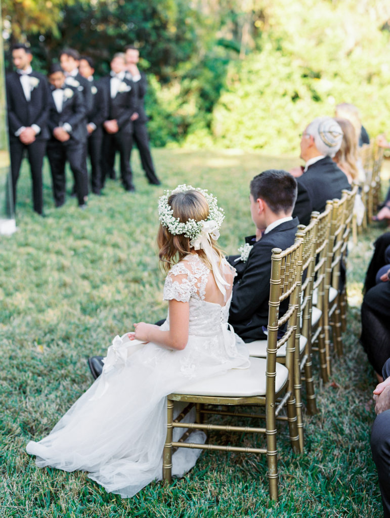 Flower girl sits and watches wedding ceremony 