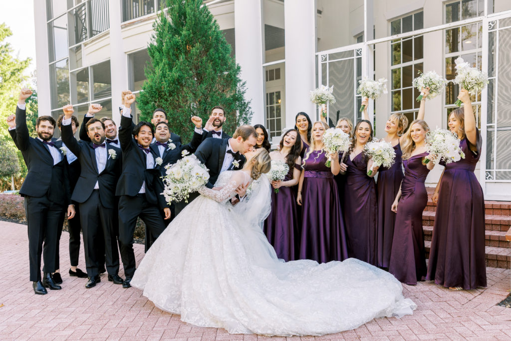 Bride and groom dip kiss in front of bridal party as they cheer 