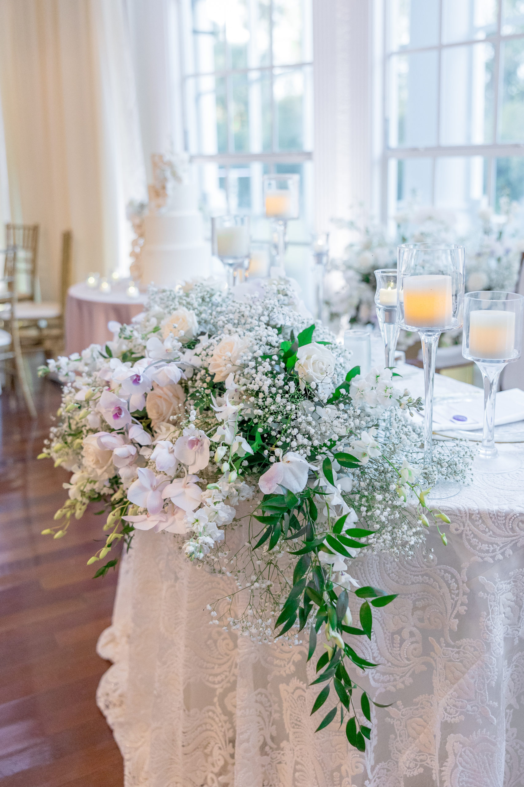 Bride and groom's wedding reception table bouquet of white roses and light purple flowers with candles in tall glasses for Luxmore Grande Wedding