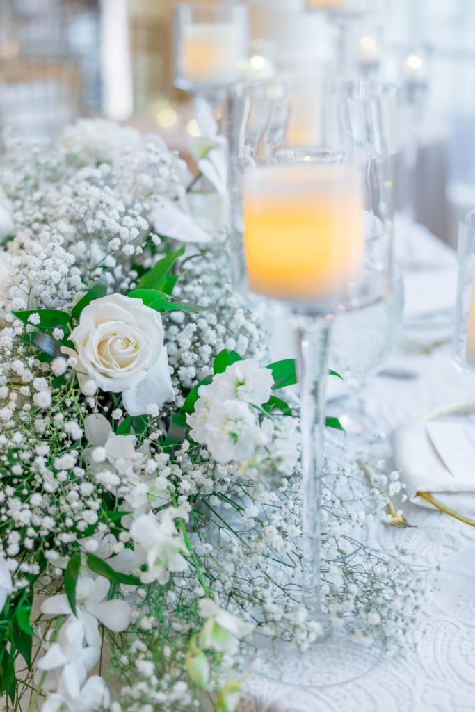 Close view of white flower arrangement and candle in tall glass for wedding reception 