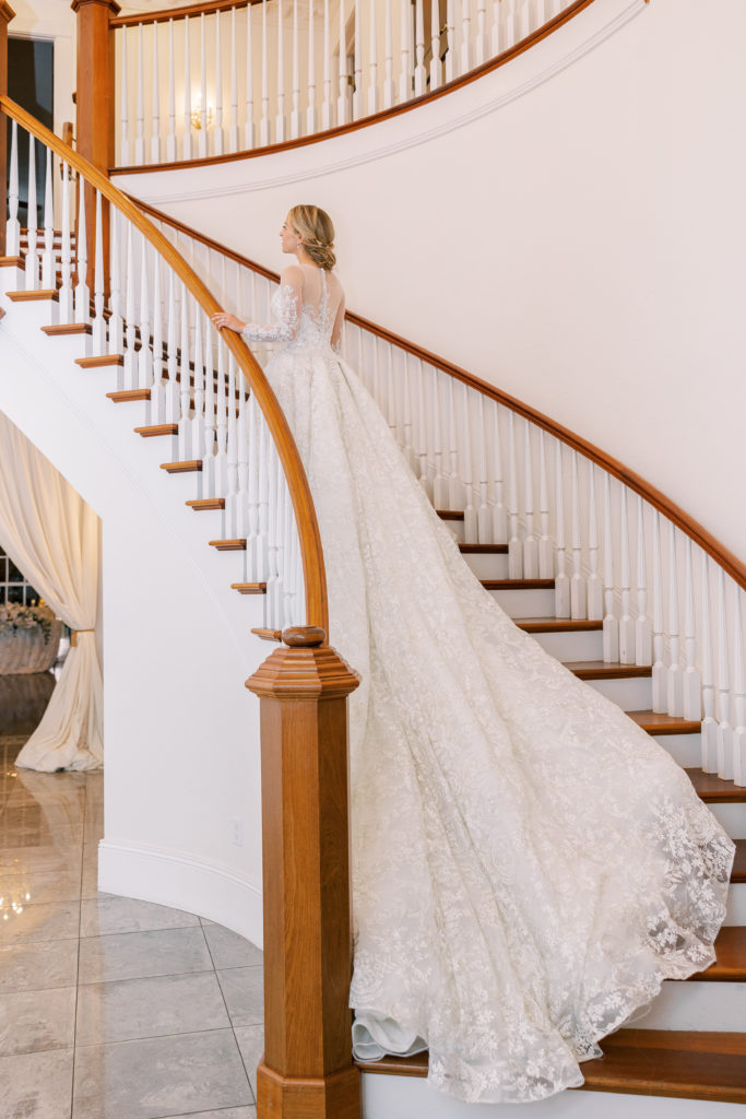 Bride walks up grand staircase holding railing as dress follows behind for Luxmore Grande Wedding