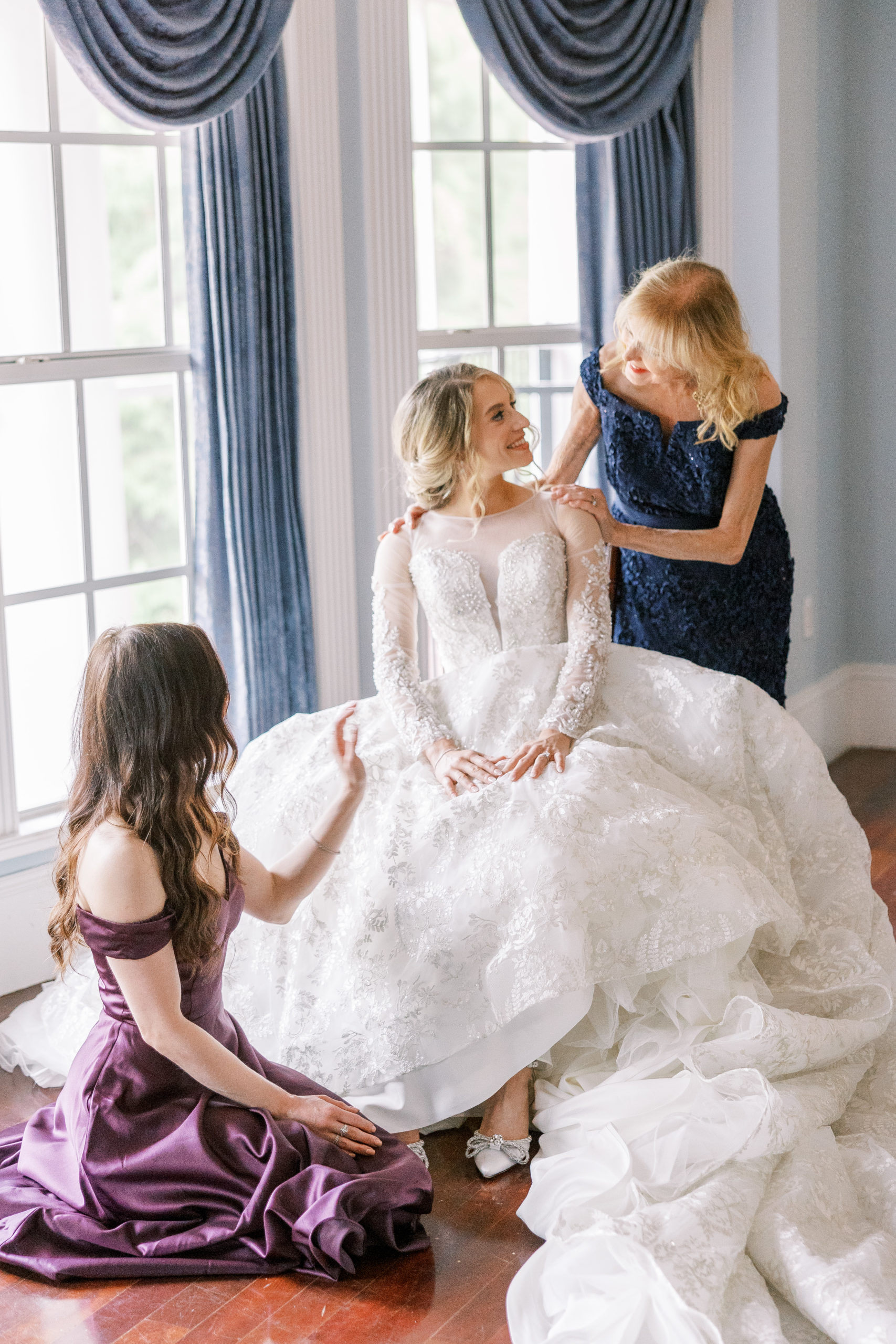 Bride sits in chair and is admired by bridesmaid and mother for Luxmore Grande Wedding