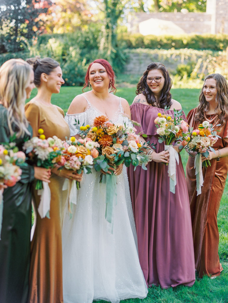 Bride smiles holding bouquet with bridesmaids on green lawn for philadelphia wedding photographer
