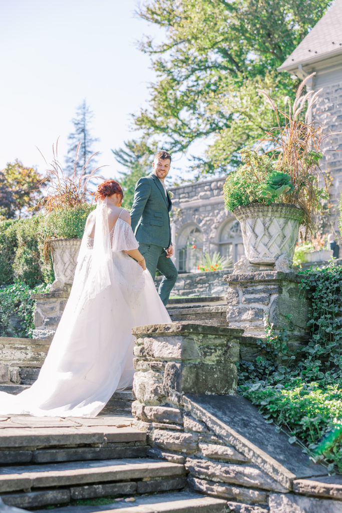 Groom leads bride up stone stairs to garden 