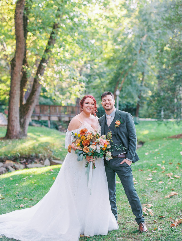 Bride and groom pose with beautiful green landscape with small wooden bridge and creek in the background for philadelphia wedding photographer