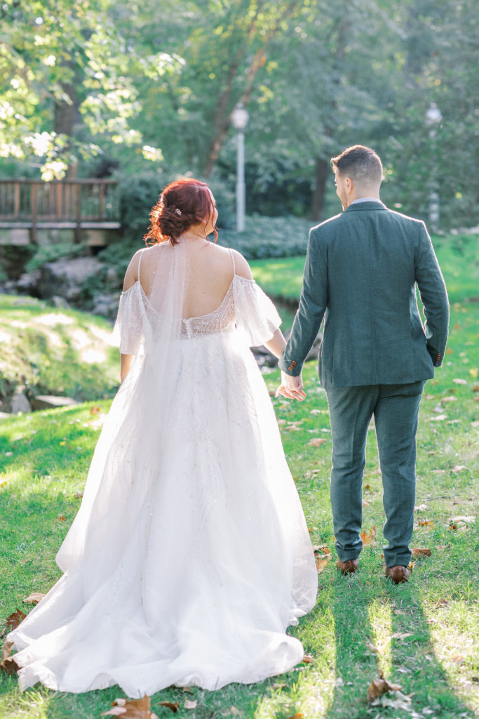 Bride and groom hold hands and admire small creek in the lawn for philadelphia wedding photographer