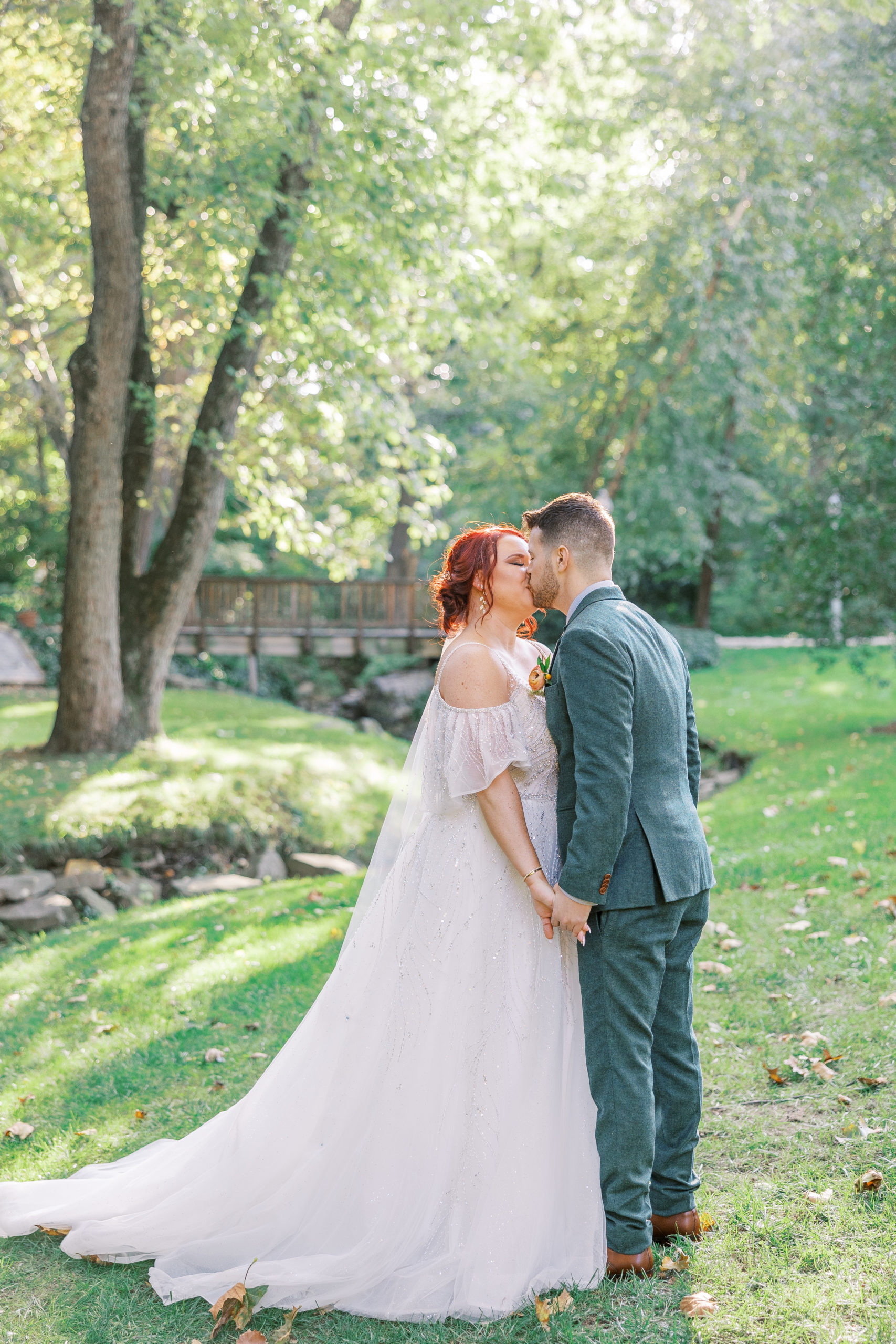 Bride and groom share a kiss and hold hands in green landscape at this pomme radnor wedding