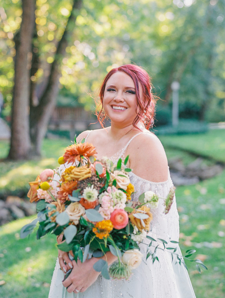Bride poses with flower bouquet of orange, pink and ivory flowers 