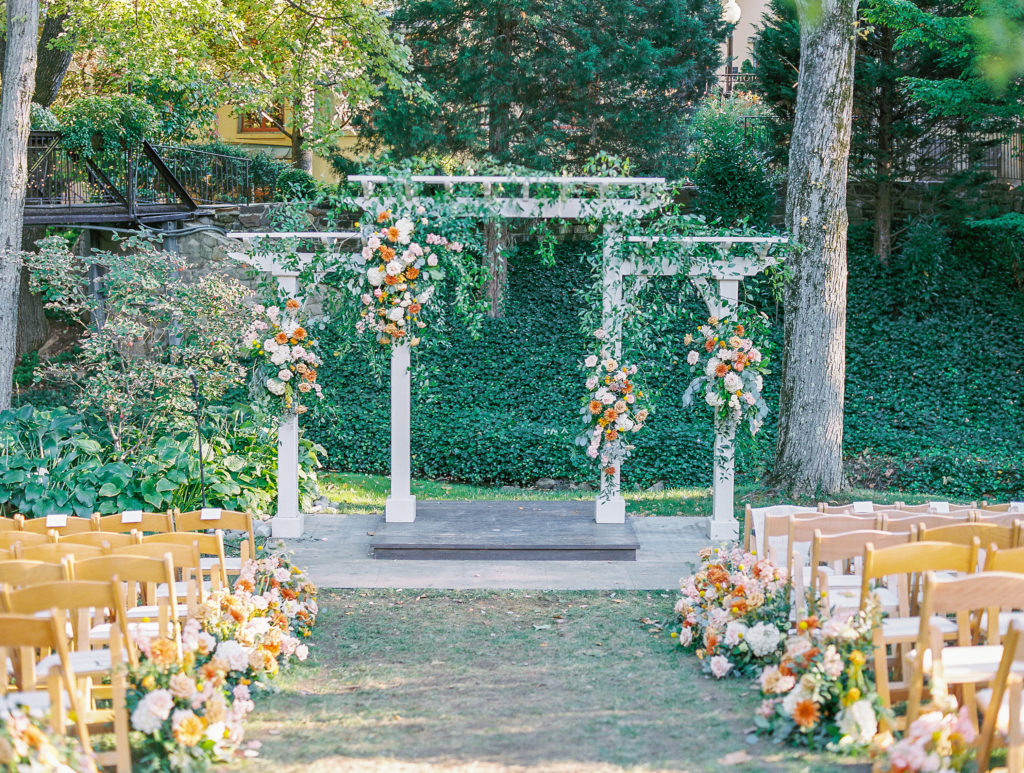 Wedding ceremony iwht white arch and large flower arrangements, and flowers lining the aisle at this pomme radnor wedding