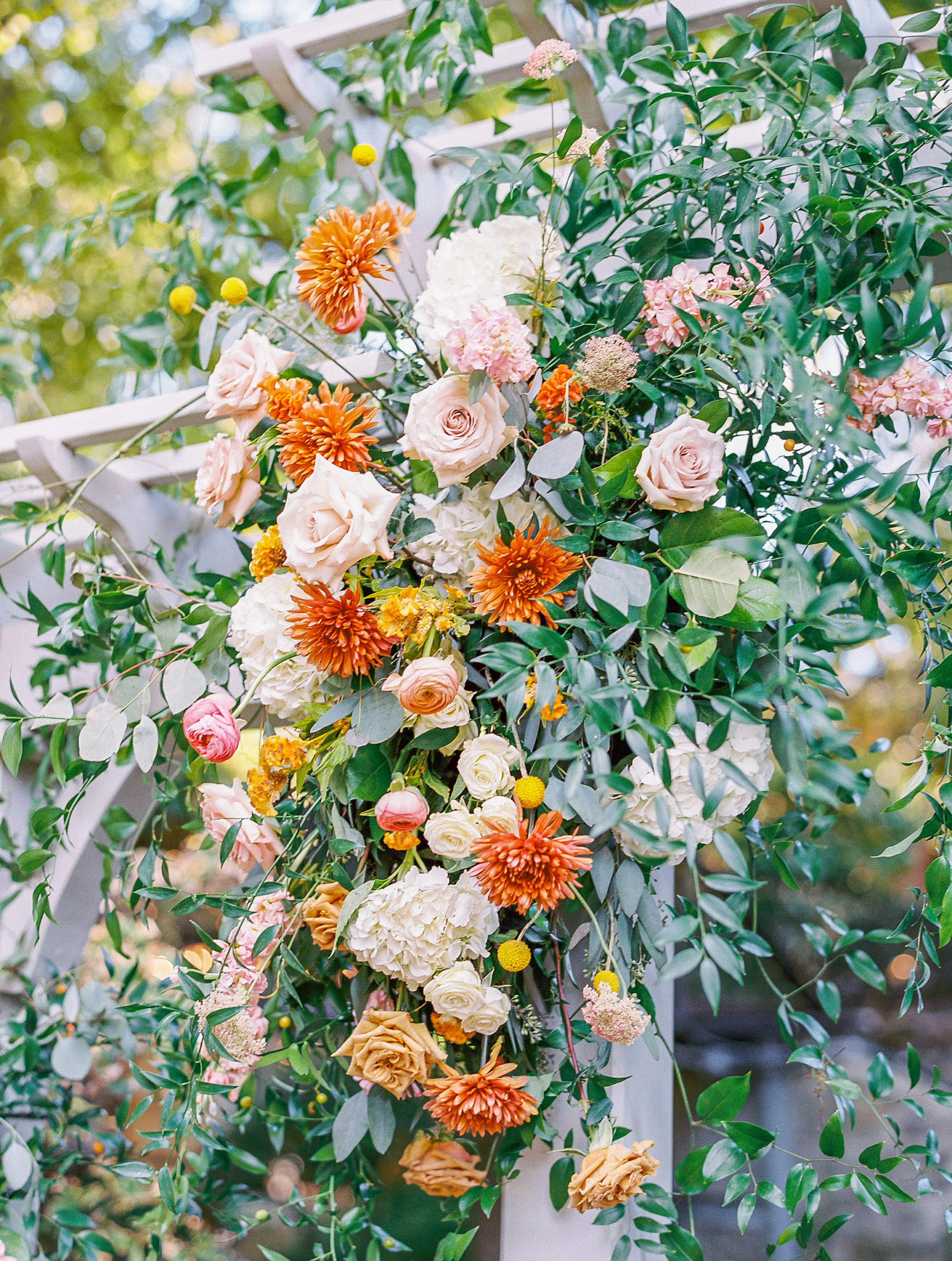 Large flower arrangement of orange, yellow, pink, and white flowers on white arch for wedding ceremony at this pomme radnor wedding