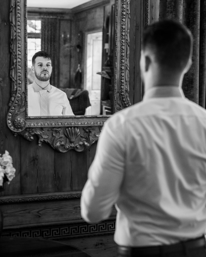Groom adjusts tie in mirror for philadelphia wedding photographer
