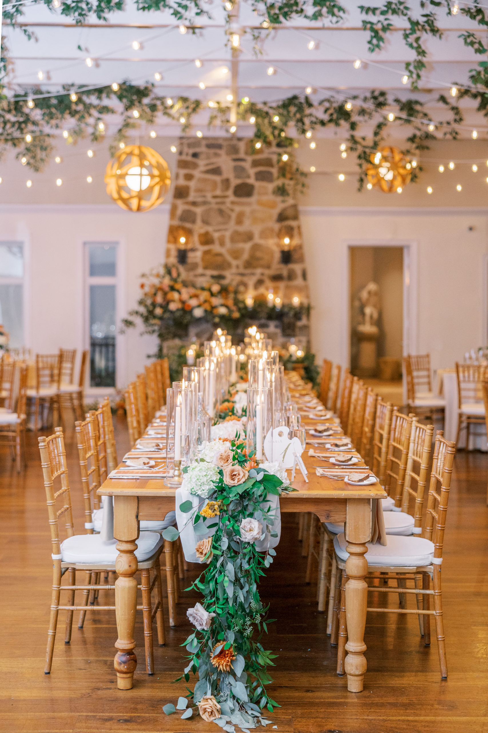 Long table for wedding reception with tall candles and white and orange flowers and leaves down the table at this pomme radnor wedding