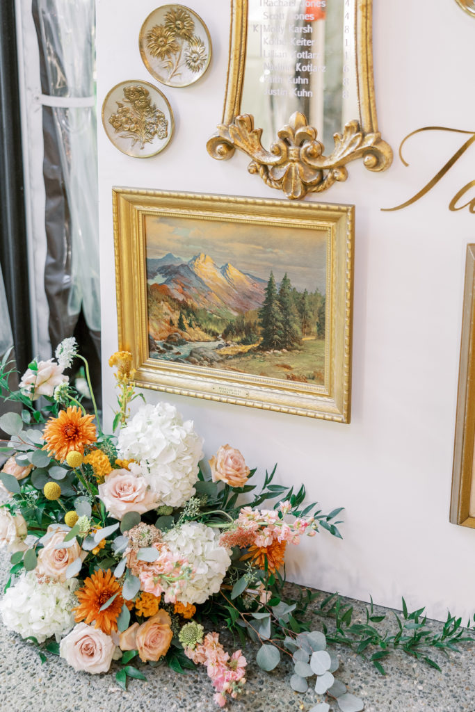 White and orange flower arrangement with gold framed painting and mirror on the wall for philadelphia wedding photographer