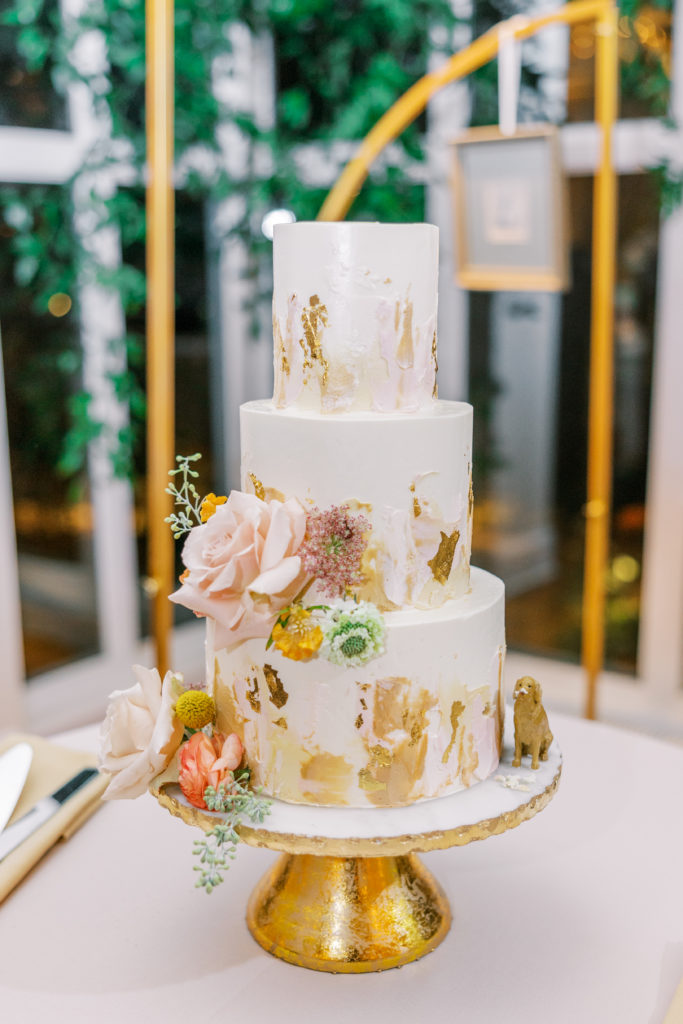 3 tiered cake with small dog figure and flowers on golden cake platter for philadelphia wedding photographer