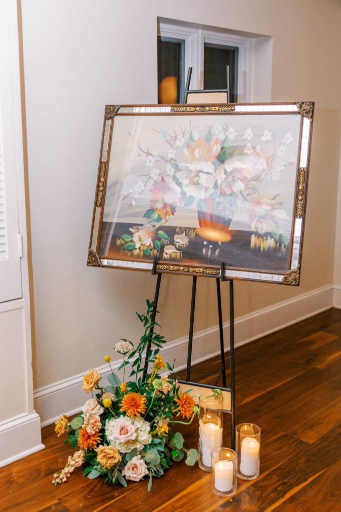 Painting on stand with flower arrangement and 3 candles on the floor 