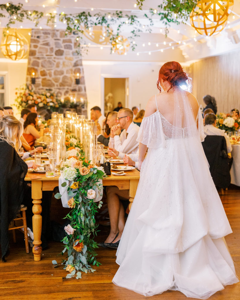 Bride stands and looks at guests at long reception table for philadelphia wedding photographer