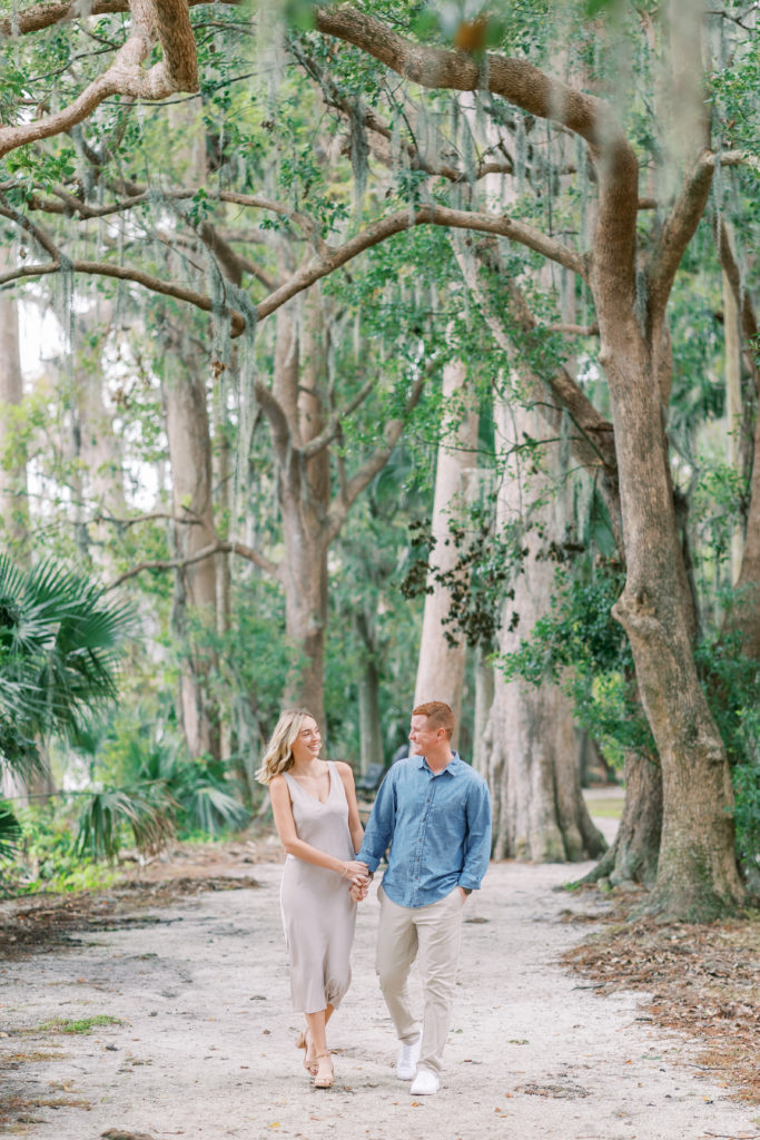 couple walks on white gravel path in Florida garden in this Winter Park Engagement Session