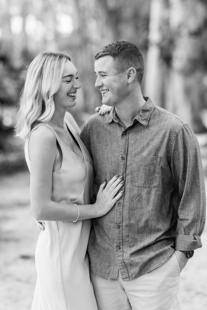 couple laughs while standing together arm in arm captured in black and white in this Winter Park Engagement Session